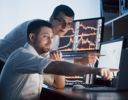 Team of stockbrokers are having a conversation in a dark office with display screens. Analyzing data, graphs and reports for investment purposes. Creative teamwork traders